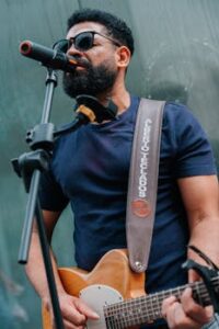 Musician performs outdoors with guitar and microphone, engaging street audience.